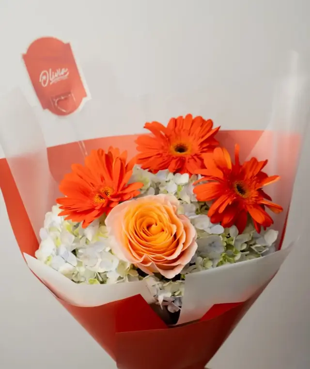 Amber Glow – Ramo de gerberas naranja, rosa color durazno e hortensia en papel naranja.
