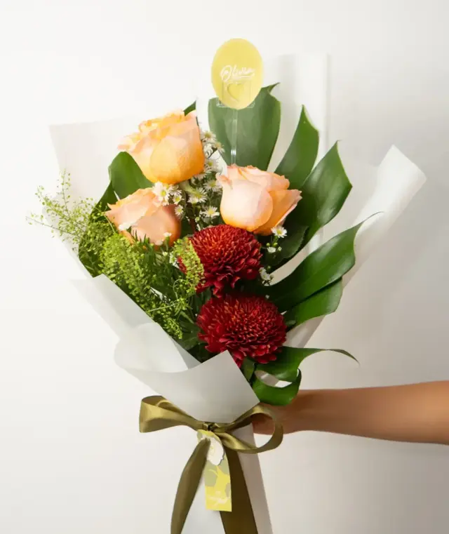 Sunset Bloom – Ramo de rosas durazno y crisantemos rojos con hojas de monstera.